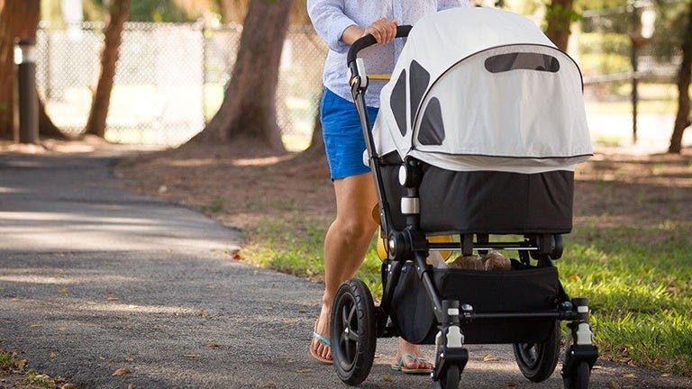 Une femme en tenue de sport se promène dans un parc avec sa poussette.