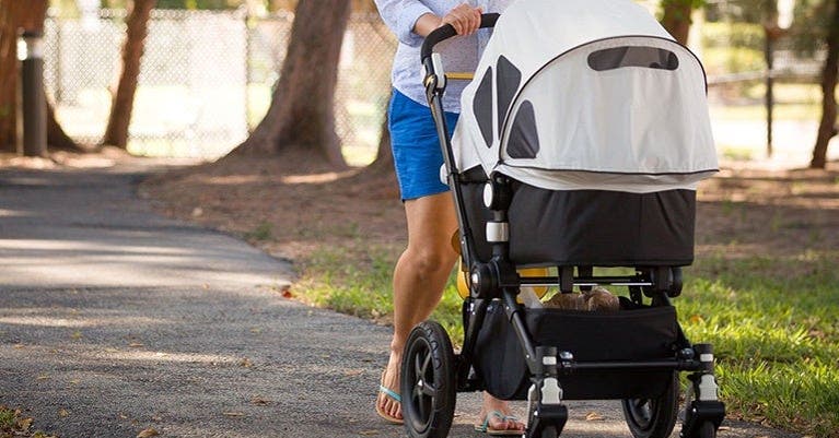 Une femme en tenue de sport se promène dans un parc avec sa poussette.