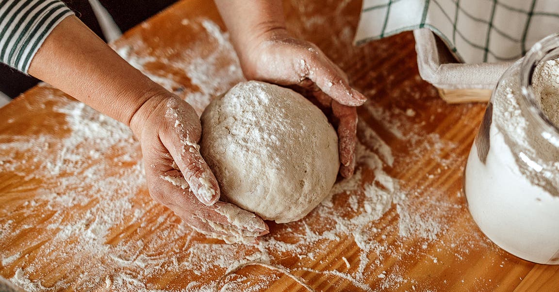 Eine Frau formt auf einer bemehlten Arbeitsfläche Teig zu einer Kugel.