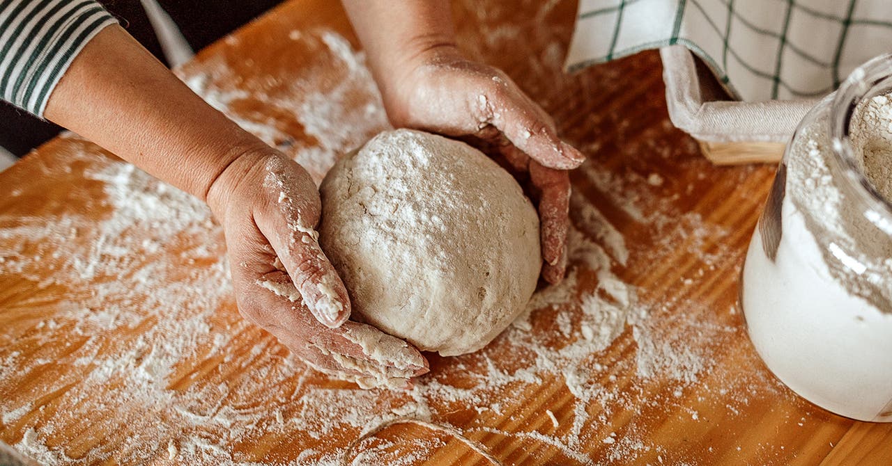 Une femme forme une boule de pâte sur une surface farinée.