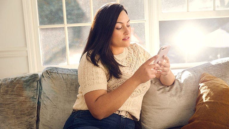 Frau sitzt auf Sofa und schaut aufs Handy