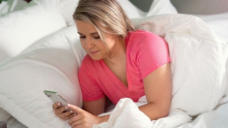 WW Mitglied Ivana schaut im Bett auf ihr Smartphone.