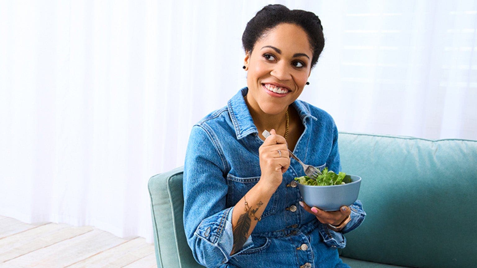 Cecilia, membre de WW, est assise sur un canapé en jean et mange une salade.