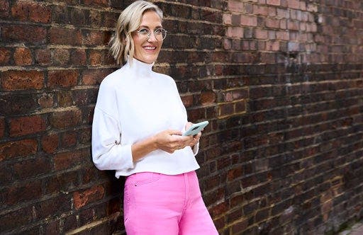 Martina, membre du WW, en t-shirt blanc, est adossée à un mur de pierre, son téléphone portable à la main.