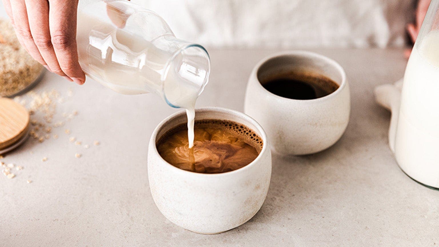 Zwei Tassen Kaffee, in die Milch gegossen wird