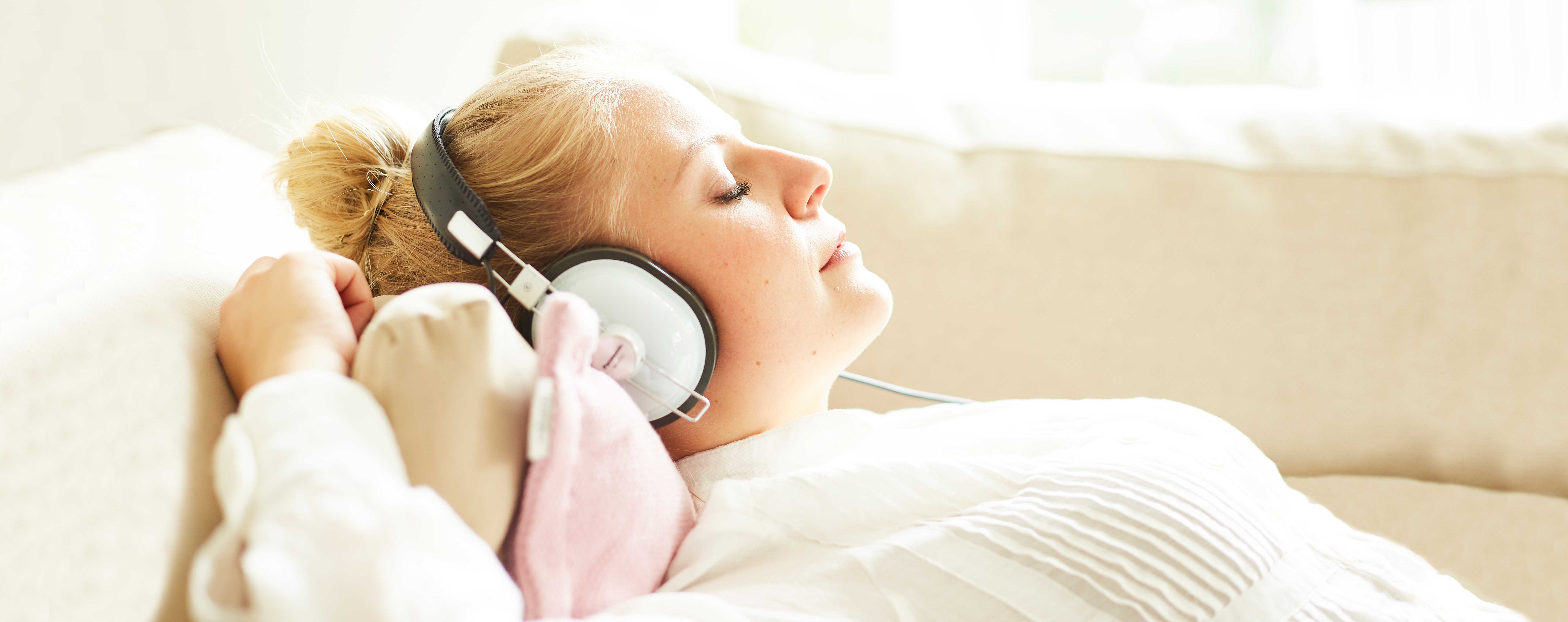 Junge Frau hört mit geschlossenen Augen auf dem Sofa Musik