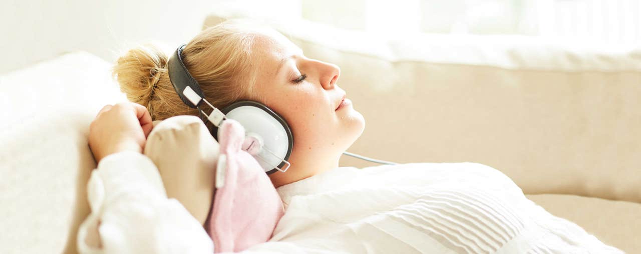 Junge Frau hört mit geschlossenen Augen auf dem Sofa Musik