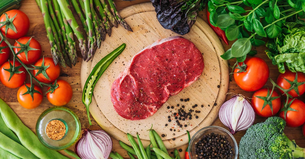 Une plaque sur laquelle se trouve un morceau de viande rouge, entouré de nombreux légumes.