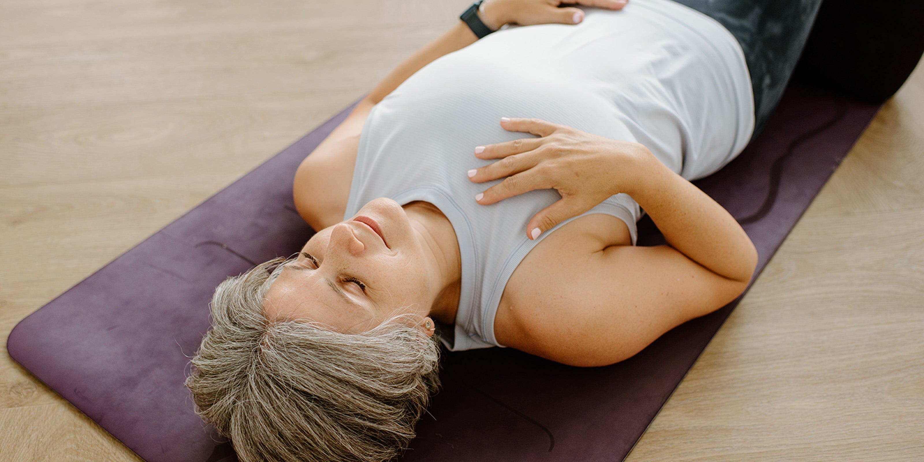 Eine Frau liegt mit geschlossenen Augen auf einer Yoga-Matte.