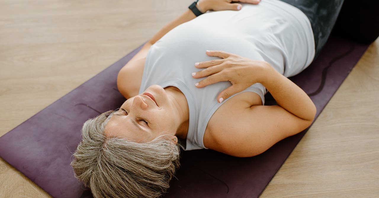 Une femme est allongée sur un tapis de yoga, les yeux fermés.