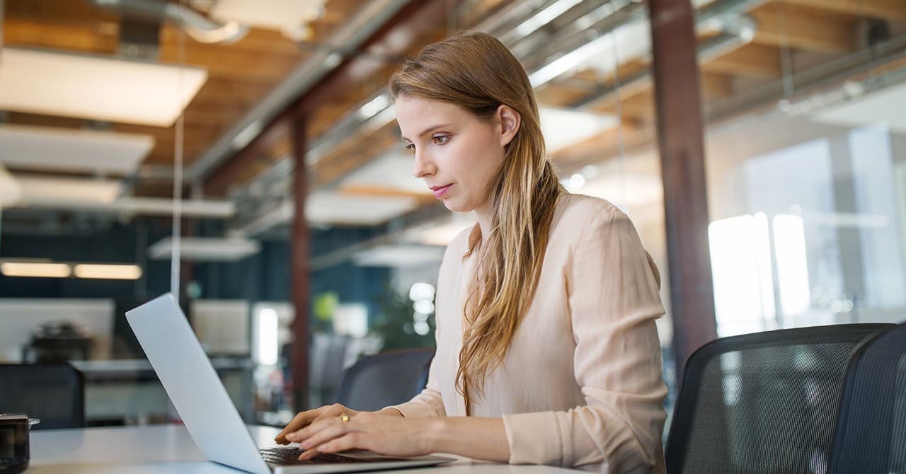 Eine junge Frau arbeitet im Büro am Laptop.