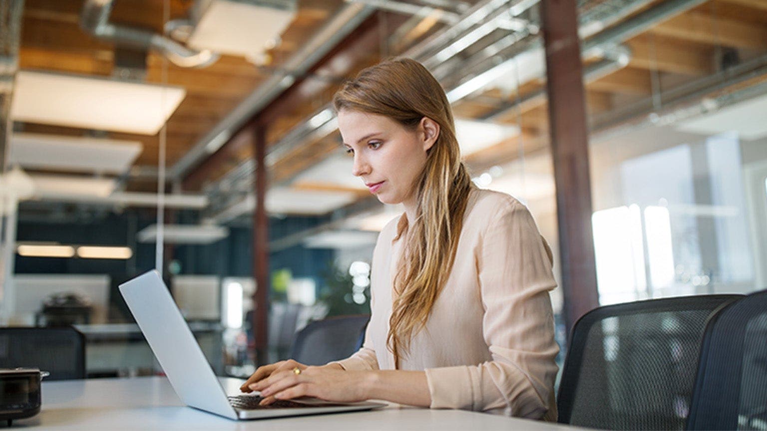 Eine junge Frau arbeitet im Büro am Laptop.