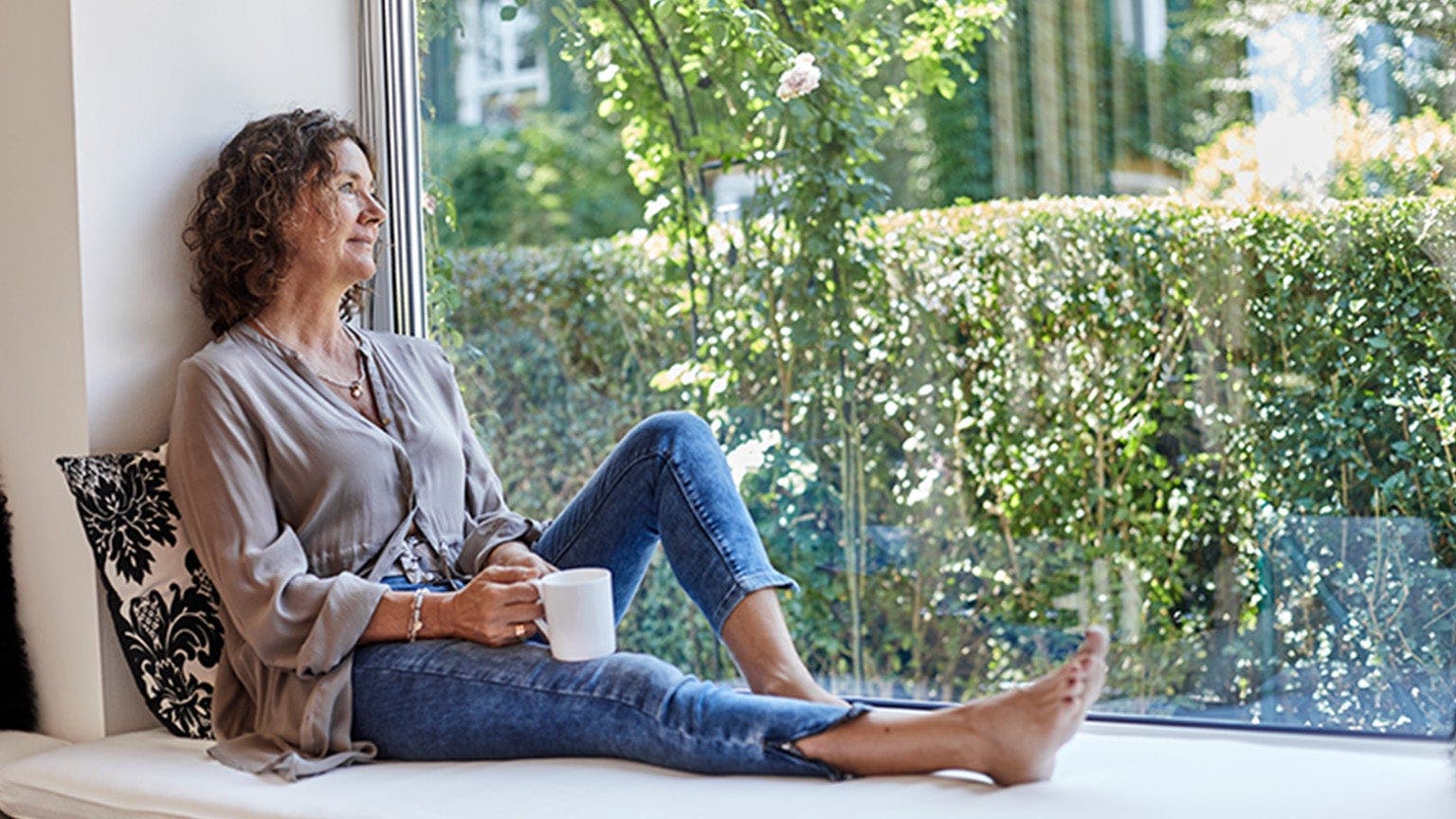 Une femme prend un café et regarde par la fenêtre.