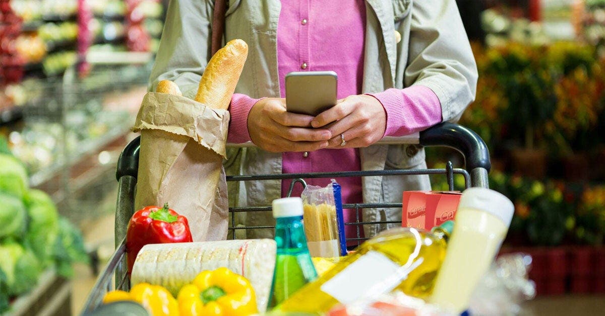 Eine Frau schiebt einen Einkaufswagen und schaut ins Handy