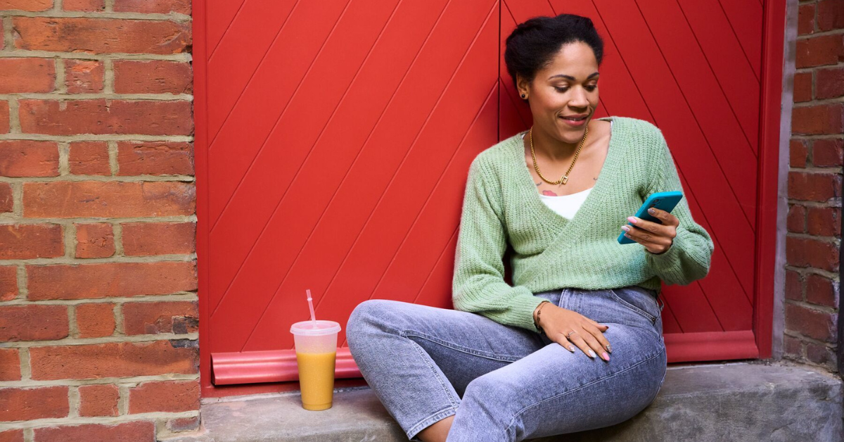 Frau sitzt vor einer Tür mit einem Handy in der Hand