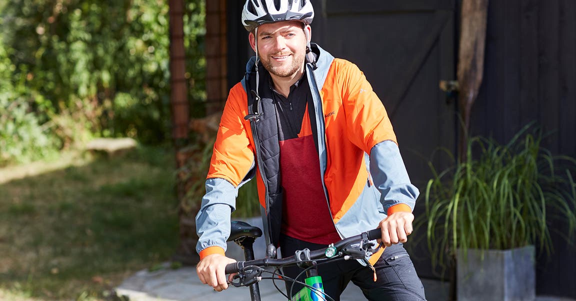Ein Mann mit Fahrradhelm und Sportkleidung steht neben seinem Fahrrad