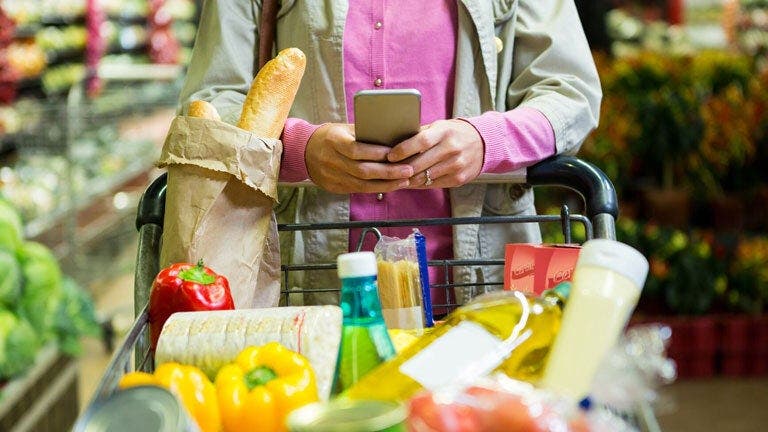 Eine Frau schiebt einen Einkaufswagen und schaut ins Handy