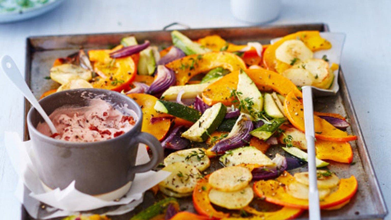 Ein Blech mit Kürbisspalten, anderem Ofengemüse und einem Tomaten-Dip