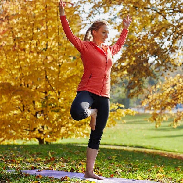 Blonde Frau steht auf einer Wiese und macht Yoga