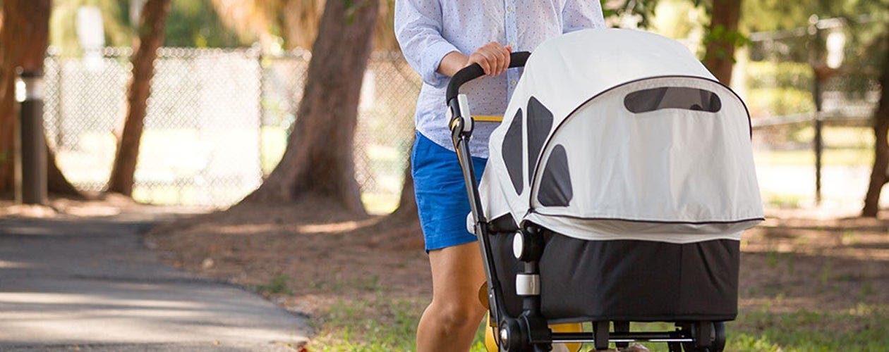 Eine Frau in Sportkleidung geht mit einem Kinderwagen im Park spazieren.