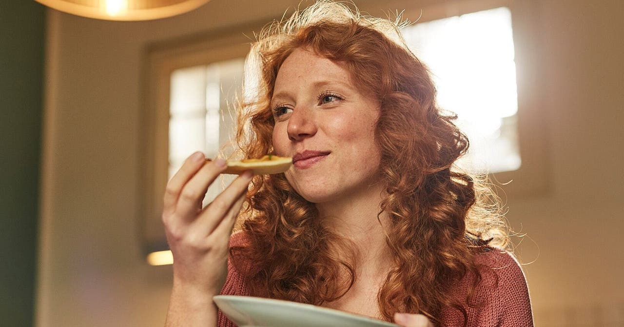 Junge Frau mit roten Haaren isst ein Stück Pizza.