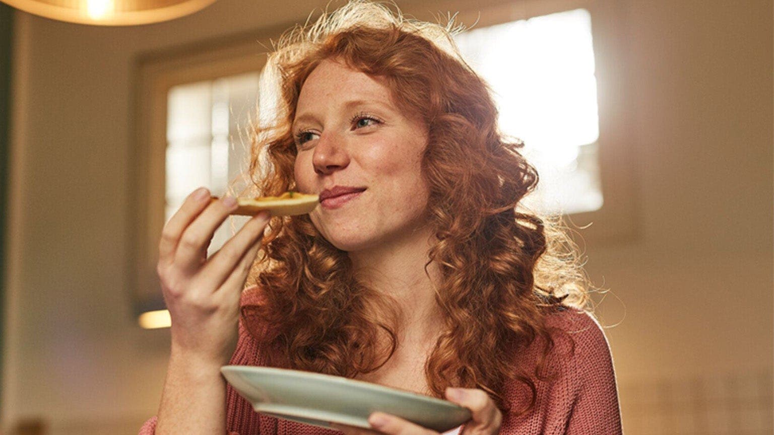 Junge Frau mit roten Haaren isst ein Stück Pizza.