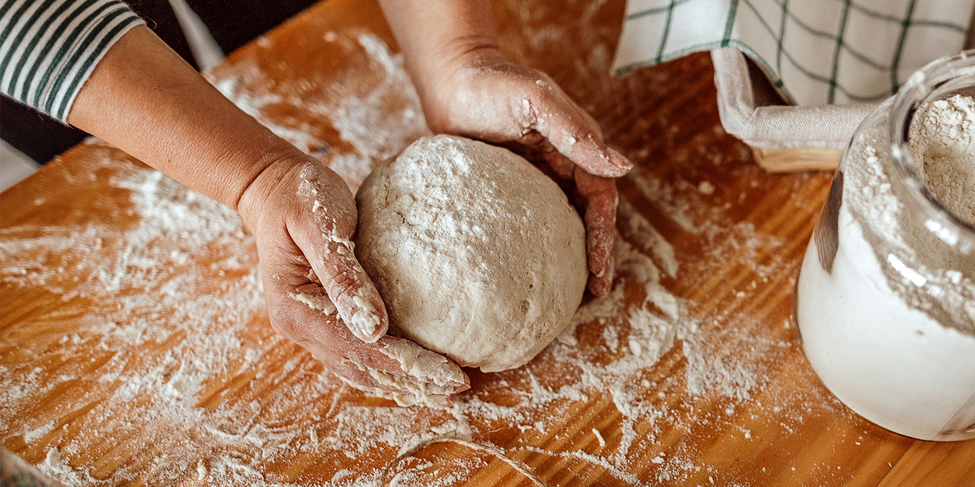 Eine Frau formt auf einer bemehlten Arbeitsfläche Teig zu einer Kugel.