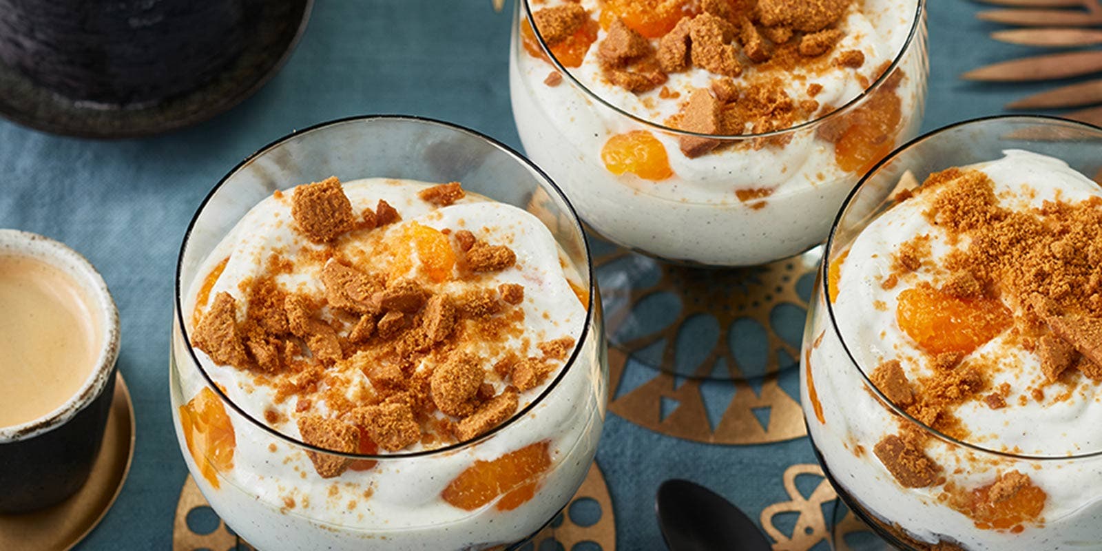 Eine Quarkspeise mit Mandarinen und Spekulatius ist auf einer weihnachtlich-festlich gedeckten Tafel angerichtet.