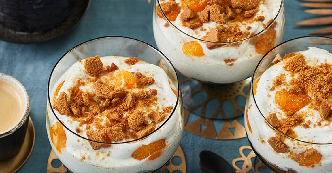 Eine Quarkspeise mit Mandarinen und Spekulatius ist auf einer weihnachtlich-festlich gedeckten Tafel angerichtet.
