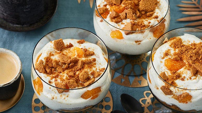 Eine Quarkspeise mit Mandarinen und Spekulatius ist auf einer weihnachtlich-festlich gedeckten Tafel angerichtet.