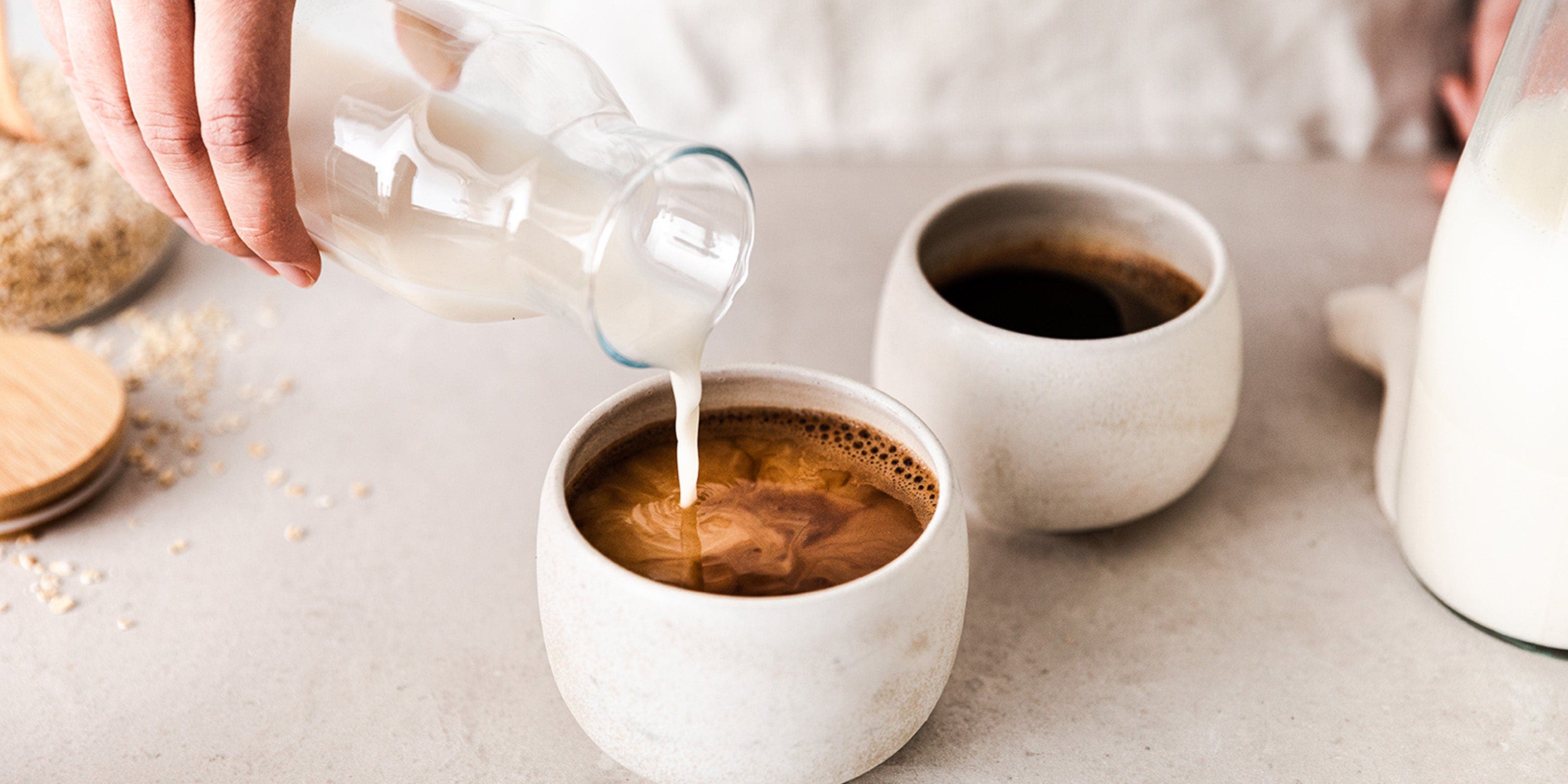 Zwei Tassen Kaffee, in die Milch gegossen wird