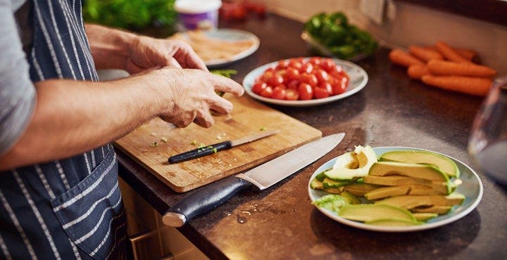 Mann mit Schürze schneidet Tomate und Avocado