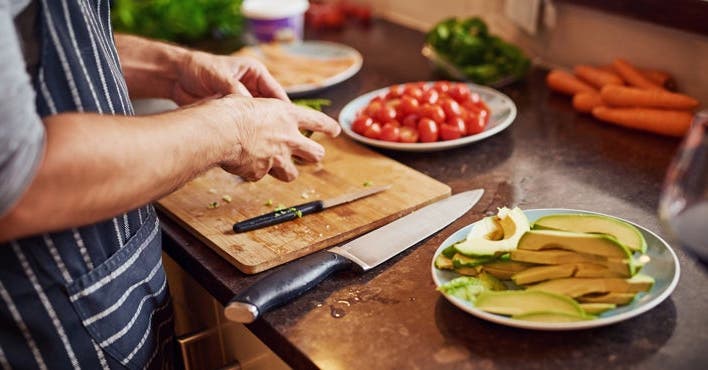 Mann mit Schürze schneidet Tomate und Avocado