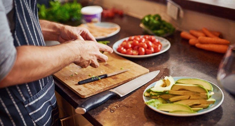 Mann mit Schürze schneidet Tomate und Avocado