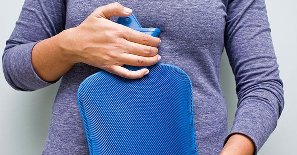 Frau hält Wärmeflasche vor ihren Bauch.