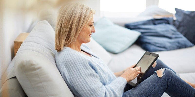 Frau mit blonden Haaren in hellblauem Pullover schaut auf Tablet 