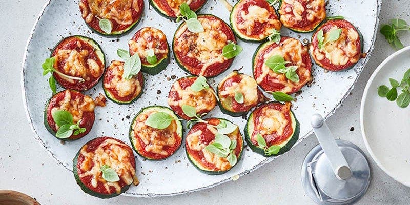 Mehrere kleine Zucchini-Pizzas mit Tomate und Basilikum auf Servierteller