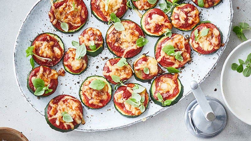 Mehrere kleine Zucchini-Pizzas mit Tomate und Basilikum auf Servierteller