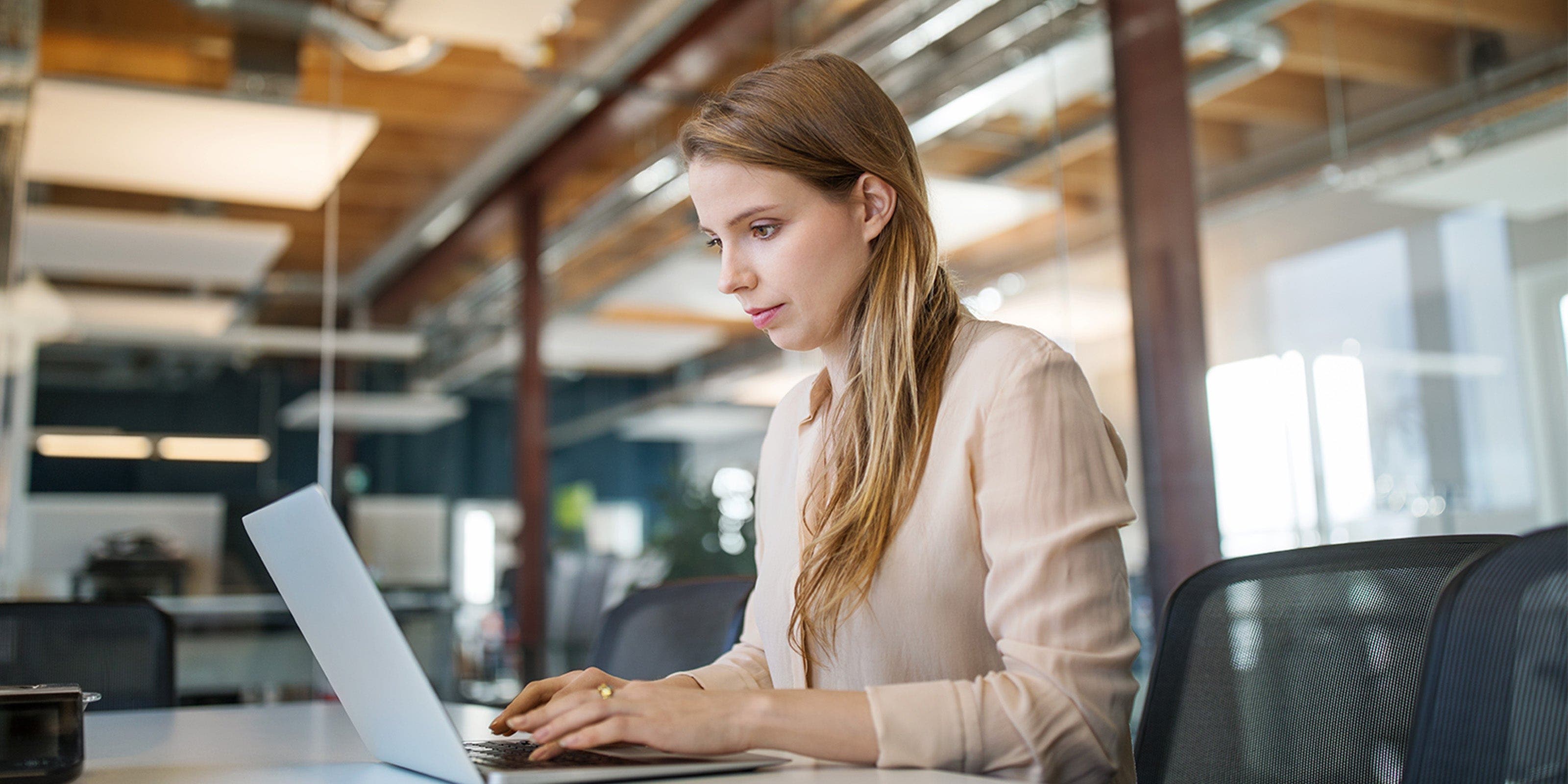 Eine junge Frau arbeitet im Büro am Laptop.