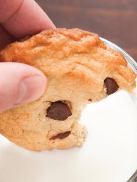 A person holding a cookie in front of a glass of milk, ready to enjoy a delightful snack.
