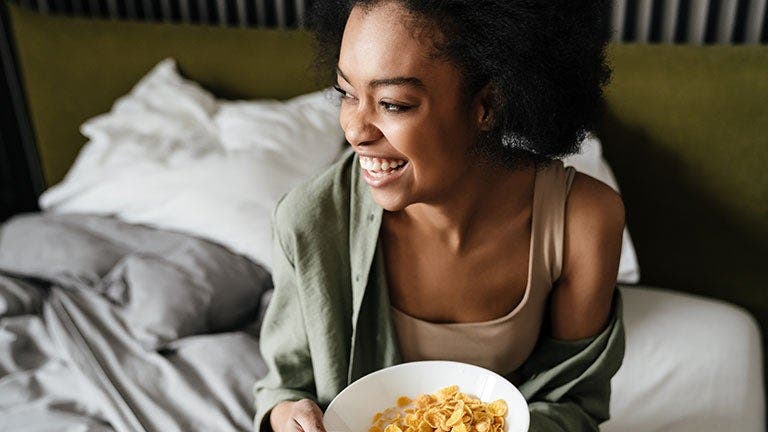 Woman sitting up in bed with a bowl of cereal