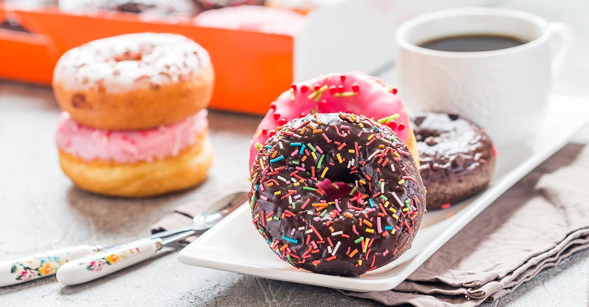 Strawberry cream–filled donut, chocolate frosted donut with sprinkles, and cup of coffee