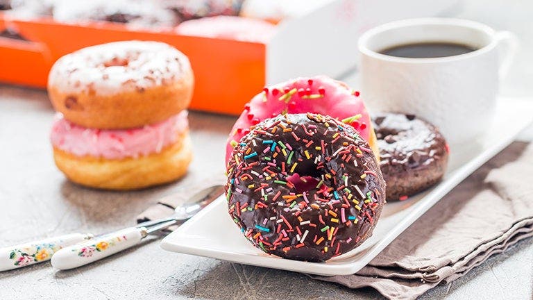 Strawberry cream–filled donut, chocolate frosted donut with sprinkles, and cup of coffee