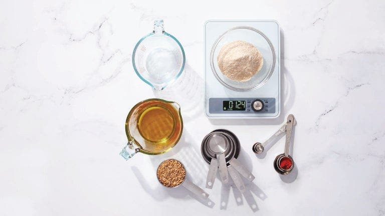 Assorted baking ingredients neatly arranged on a scale, including flour, sugar, eggs, and butter.