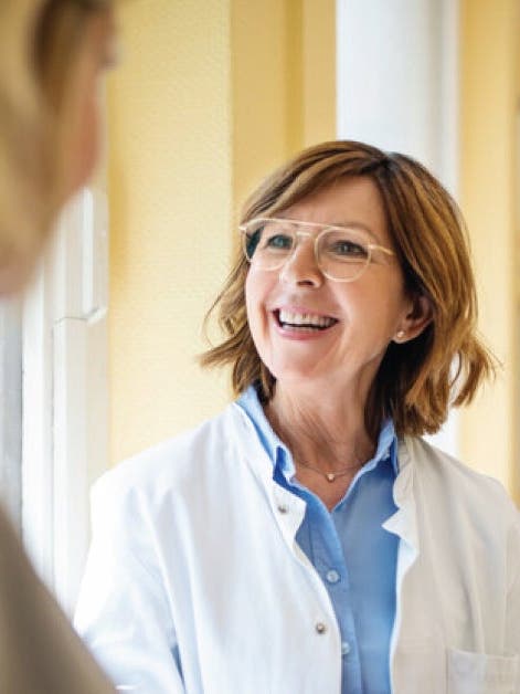 A woman in a white coat conversing with another woman.