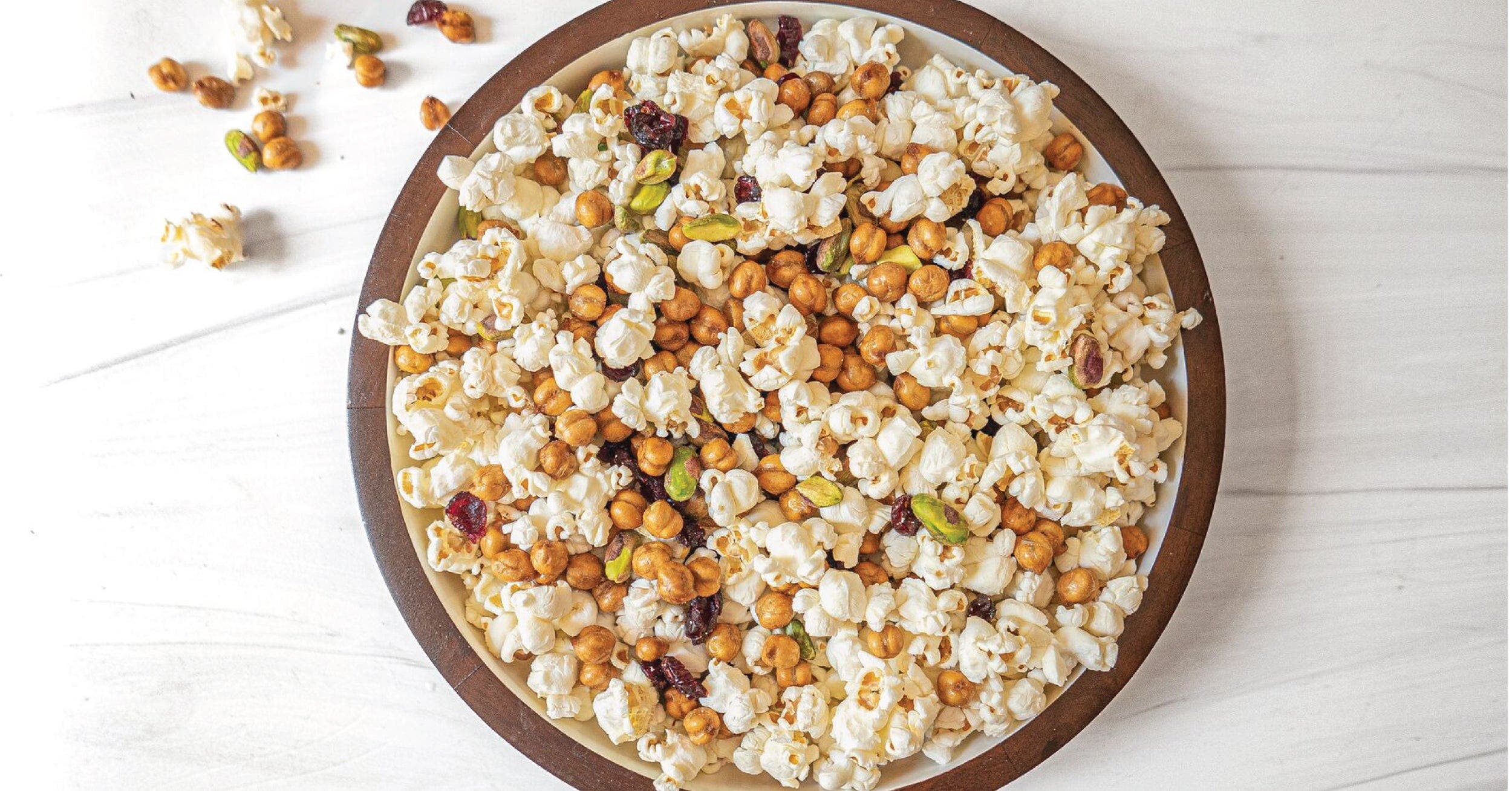  A bowl of popcorn with nuts on a white table.