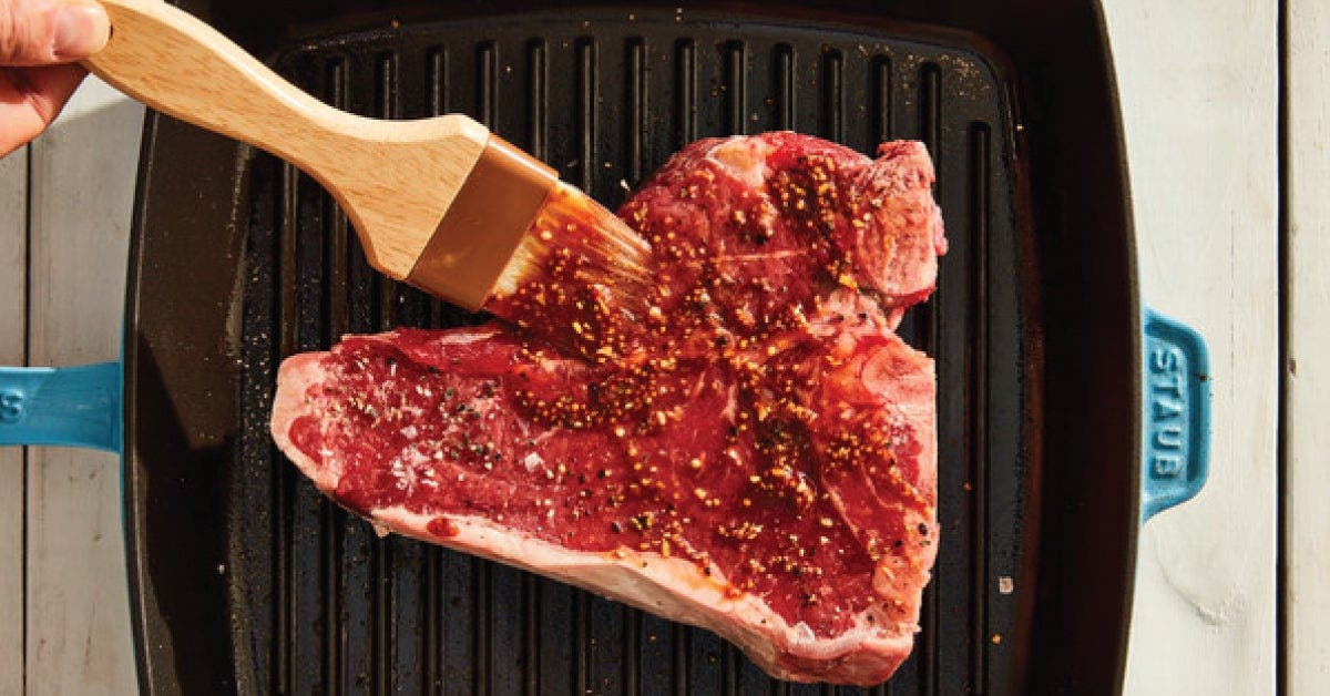 A person holding a spatula over a steak, ready to cook it to perfection on a sizzling hot grill.