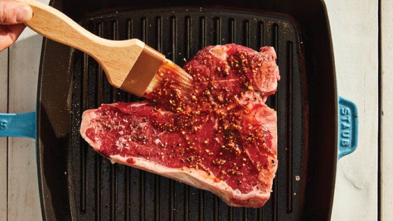 A person holding a spatula over a steak, ready to cook it to perfection on a sizzling hot grill.