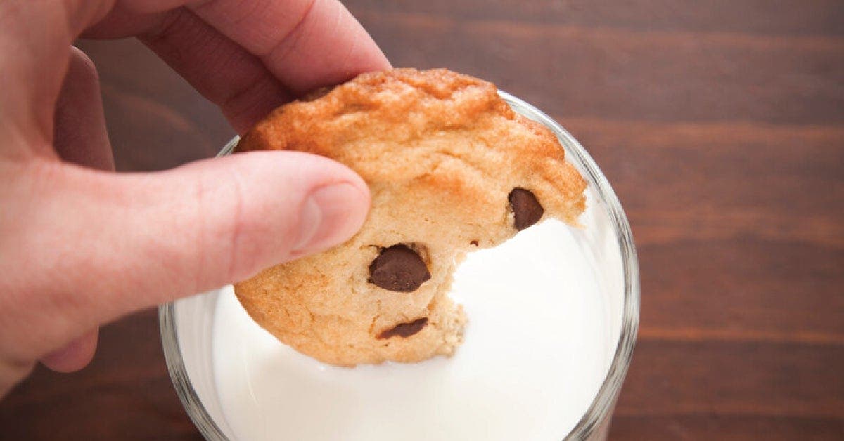 A person holding a cookie in front of a glass of milk, ready to enjoy a delightful snack.