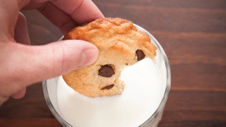 A person holding a cookie in front of a glass of milk, ready to enjoy a delightful snack.